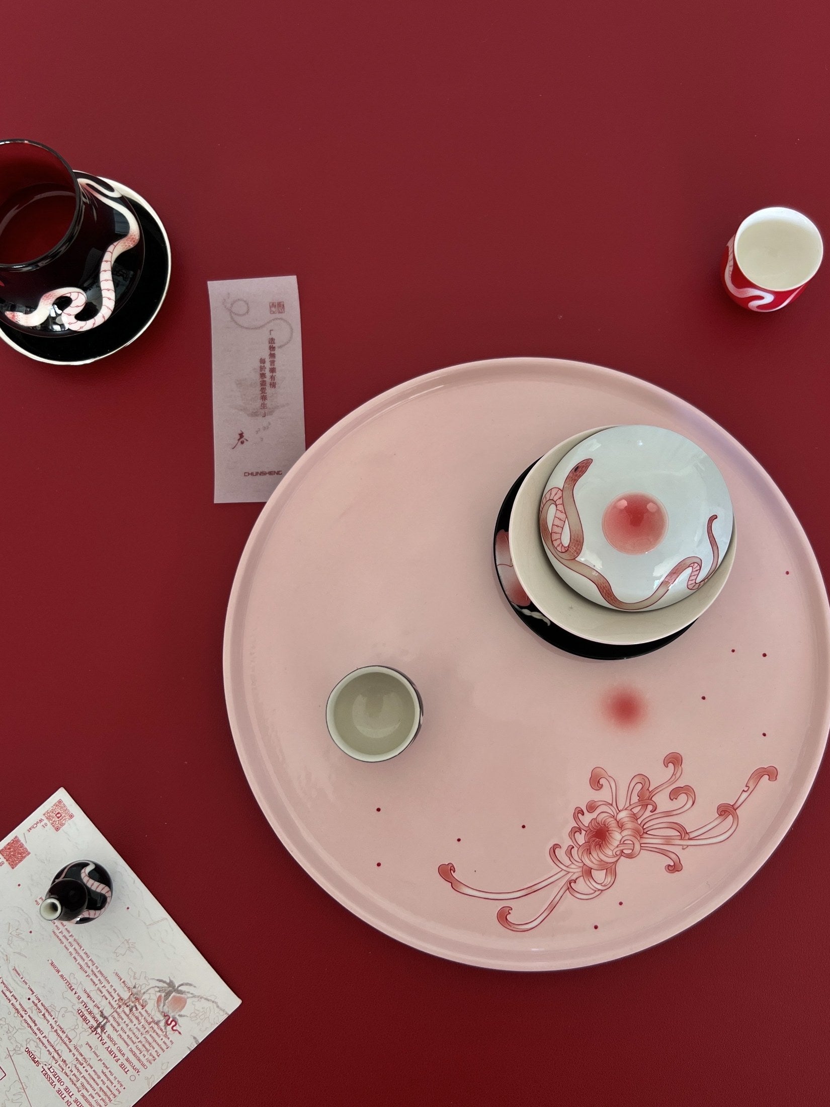 Pink hand-painted ceramic plate and serpent-decorated vessels on a rouge table, xiangong-laoshi-017